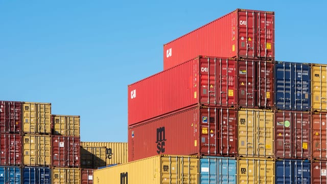 A vibrant collection of stacked shipping containers under a clear, blue sky. Ideal for logistic themes.