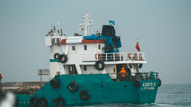 Unrecognizable people on deck of green and white vessel floating on rippling sea against gray sky