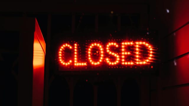 Bright red neon closed sign illuminating a dark space, conveying closure and night ambiance.