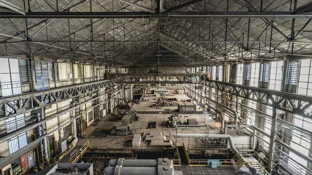 A wide-angle view of a spacious industrial warehouse interior with steel structures and machinery.