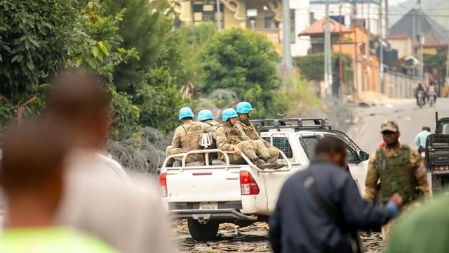 UN peacekeepers patrol a street in an urban setting, depicted with soldiers in blue helmets.