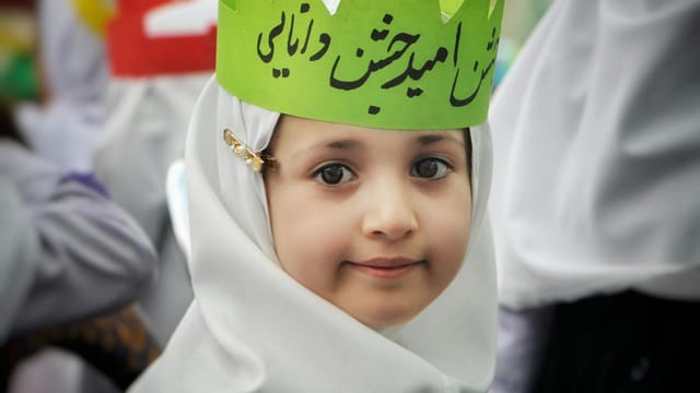 Portrait of a young girl in traditional white attire and green crown during a cultural event in Tehran.