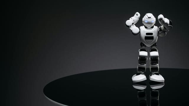 A small humanoid robot with glowing eyes on a reflective table in a dark setting.