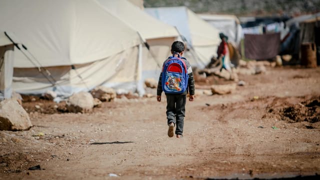 A young boy carrying a backpack walks in a refugee camp in Idlib, Syria.