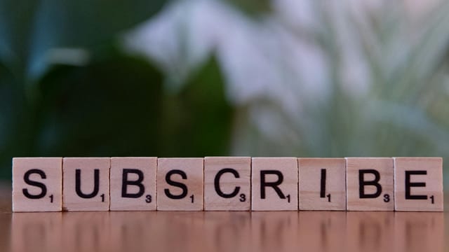 Close-up of the word 'SUBSCRIBE' spelled with wooden letter tiles on a table.