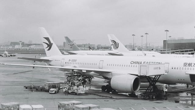 Black and white photograph of airplanes parked at an airport tarmac on a cloudy day.