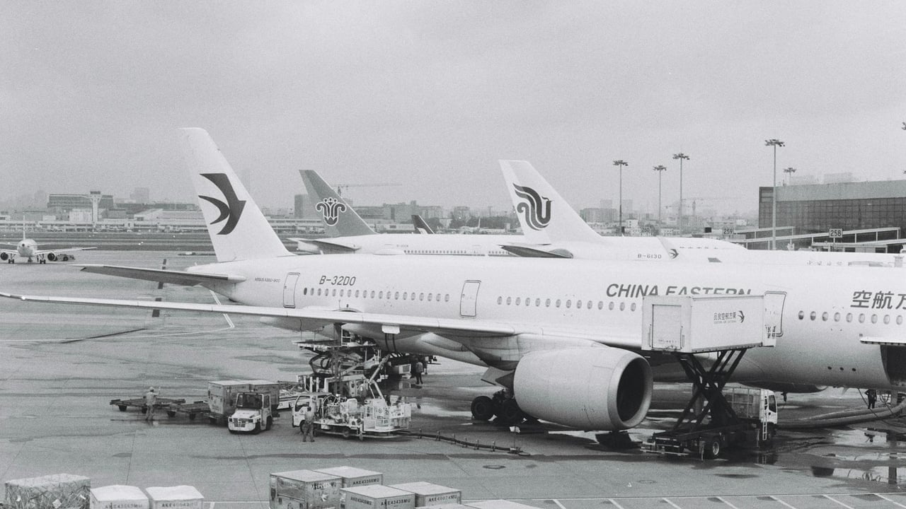 Black and white photograph of airplanes parked at an airport tarmac on a cloudy day.