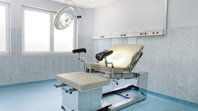 Bright gynecological examination room with adjustable chair and overhead light in a medical facility.