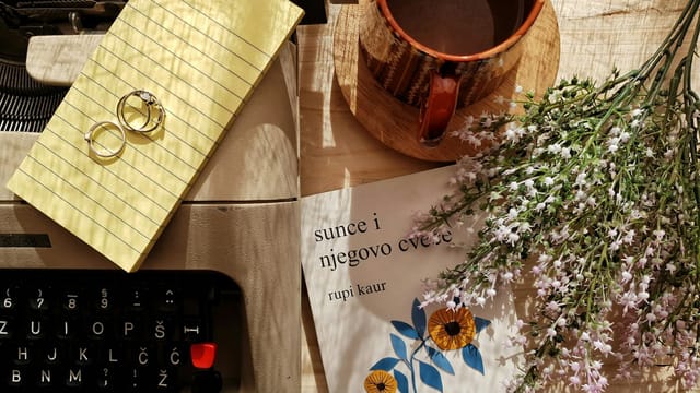 Charming vintage flatlay with a typewriter, coffee mug, flowers, and rings on a wooden surface.