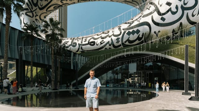 Man stands in front of Dubai's Museum of the Future, showcasing modern architecture.