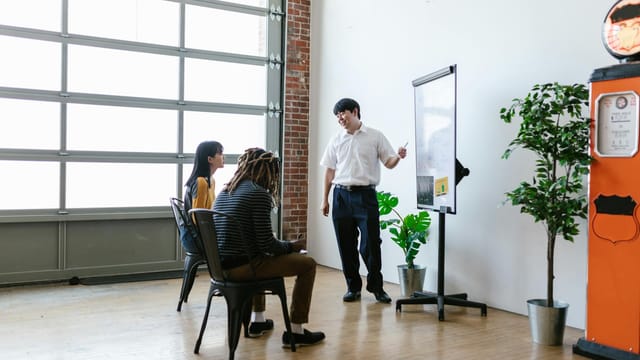 A meeting in a modern office with a presenter explaining concepts on a whiteboard.