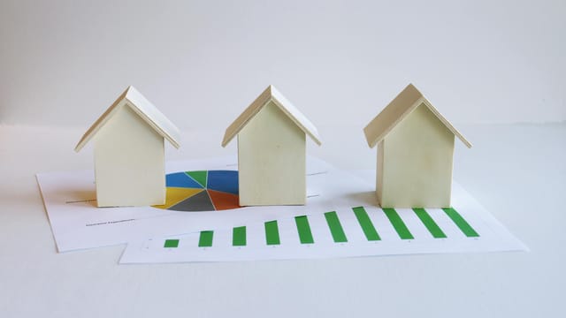 Wooden model houses on graphs depict real estate market analysis and trends.
