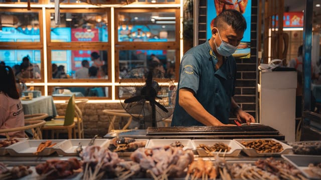 Street vendor in Guilin, China, grilling skewers in a bustling market setting.