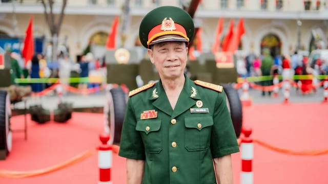 A smiling Vietnamese military officer poses at a patriotic outdoor event with red flags.