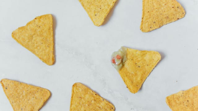 Flat lay of crunchy tortilla chips with guacamole on a white surface, perfect snack idea.