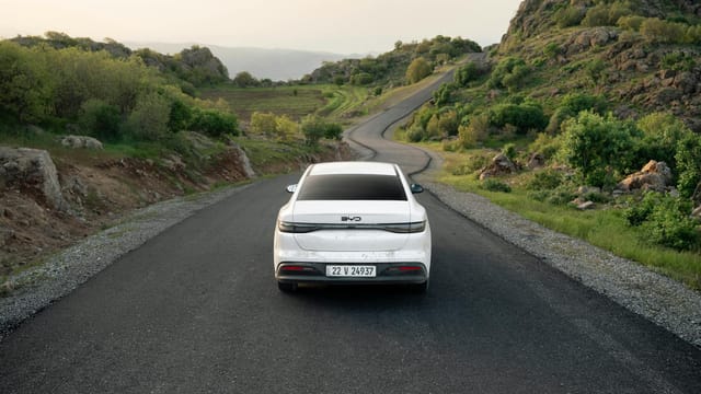 A white car travels down a winding road in the lush hills of Shaqlawa, Iraq, showcasing serene scenery.