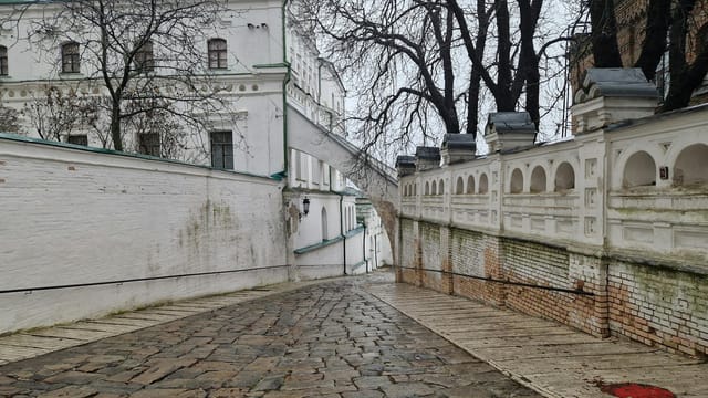 Quiet cobblestone alley beside white historical building with archways and trees.