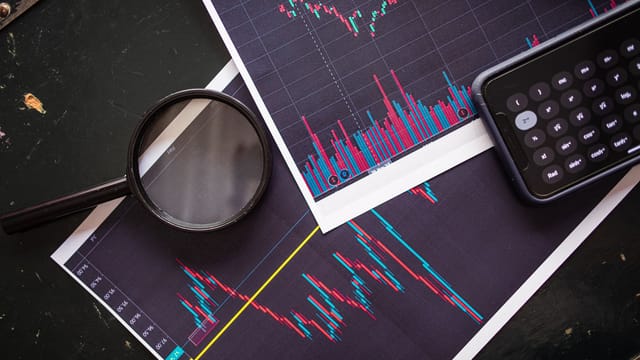 Stock market charts analyzed with a magnifying glass and calculator for financial research.