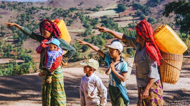 A rural family in Myanmar pointing in the countryside with baskets.
