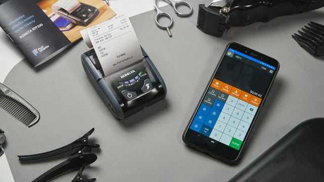 A mobile point-of-sale system in a barbershop featuring a smartphone and printer amidst salon tools.