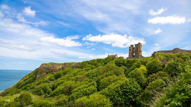 A scenic view of Scarborough Castle ruins with lush greenery and ocean backdrop.
