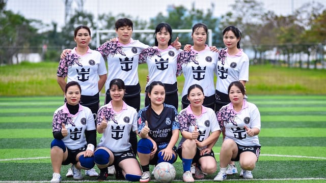 Group of women football players posing on a field in Hanoi, Vietnam, showcasing team spirit.