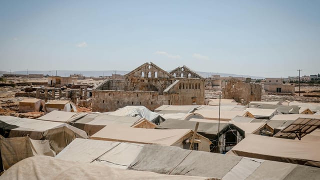 Ruins and temporary shelters in Idlib, Syria under a clear sky.