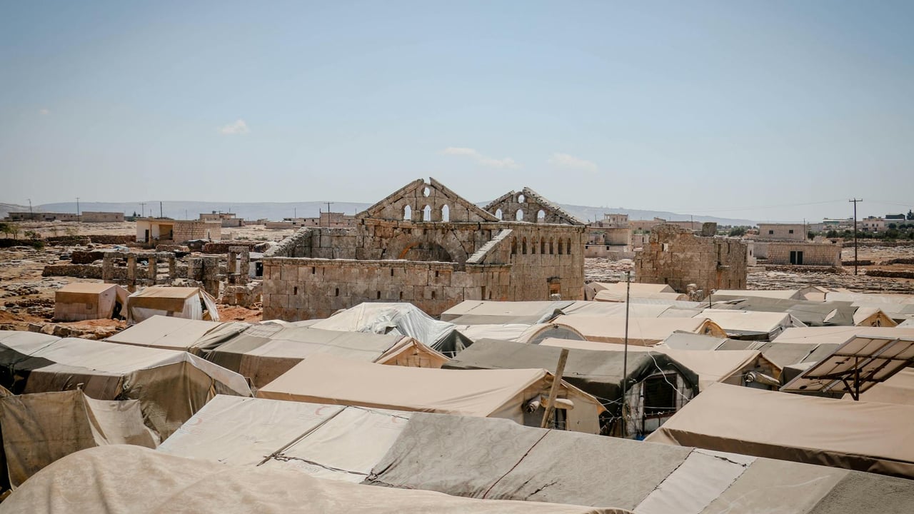 Ruins and temporary shelters in Idlib, Syria under a clear sky.