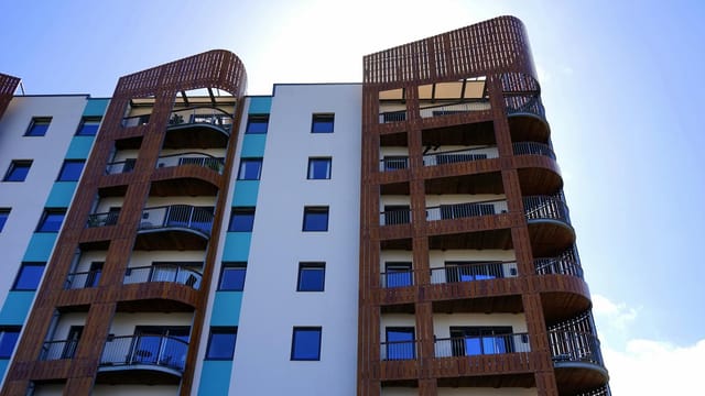 Explore the contemporary design and architecture of urban apartments with wooden accents and blue sky backdrop.