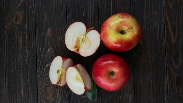 A top view of fresh red apples, whole and sliced, on a dark wooden table.