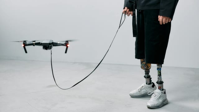 A man with prosthetic legs controls a drone indoors, showcasing innovation and modern technology.
