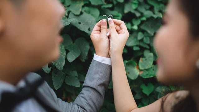 Close-up of a couple holding wedding rings with lush green background, symbolizing love and unity.