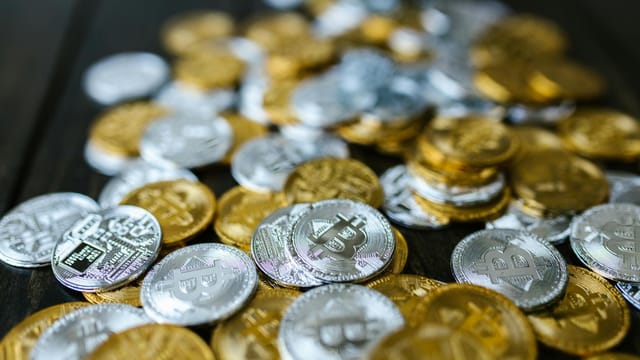 A collection of gold and silver cryptocurrency coins including Bitcoin and Ethereum on a dark surface.