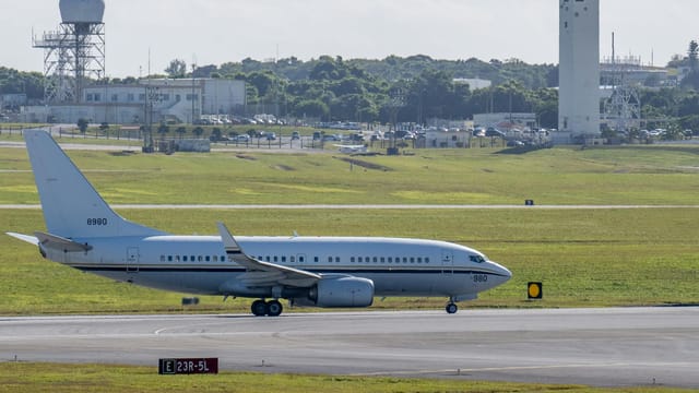 Commercial airplane taxiing on airport runway with control tower background in daylight.