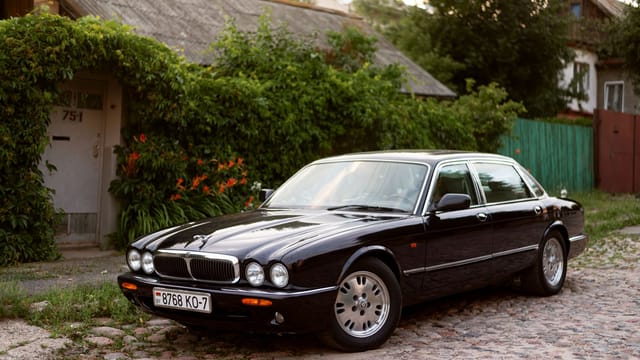 Classic Jaguar XJ car parked in a serene outdoor setting with lush greenery.