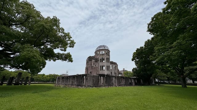 View of the iconic Hiroshima Peace Memorial amidst lush greenery and a cloudy sky.