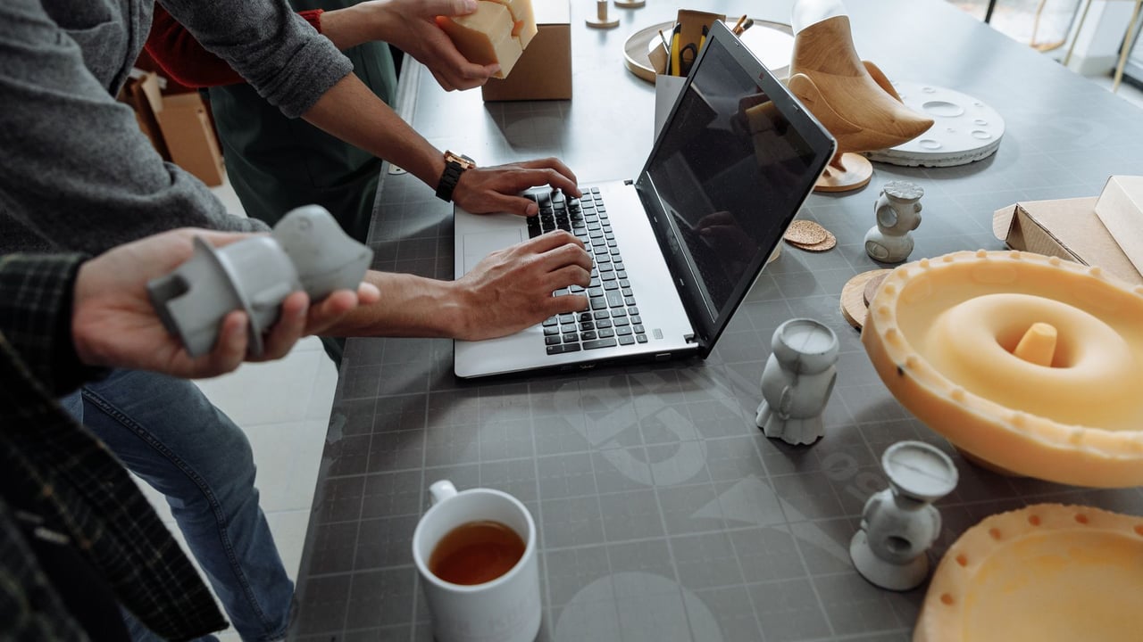 Hands on laptop in a creative workspace with 3D models and prototypes.