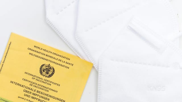 A WHO vaccination card alongside KN95 masks on a white surface, symbolizing health protection and safety.
