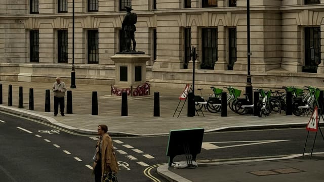 Street scene with pedestrians and statue at a historic building in London, UK.