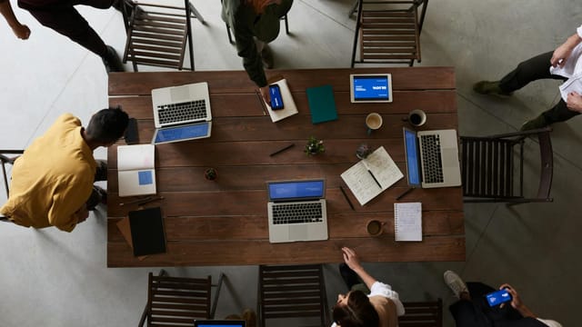 Overhead view of a team brainstorming around a table with laptops and notebooks in an office setting.