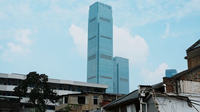 Modern skyscrapers tower over old dilapidated buildings, illustrating urban contrast.