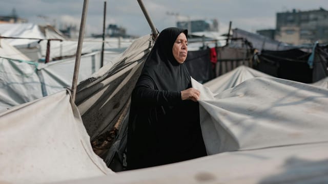 Middle Eastern woman in Gaza camp maintaining tents, symbolizing resilience amidst conflict.