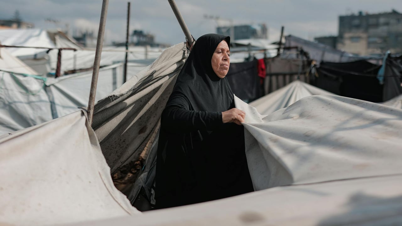 Middle Eastern woman in Gaza camp maintaining tents, symbolizing resilience amidst conflict.