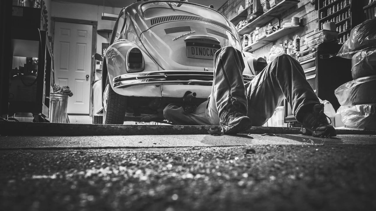 Mechanic working beneath a classic Volkswagen Beetle in a vintage garage setting.