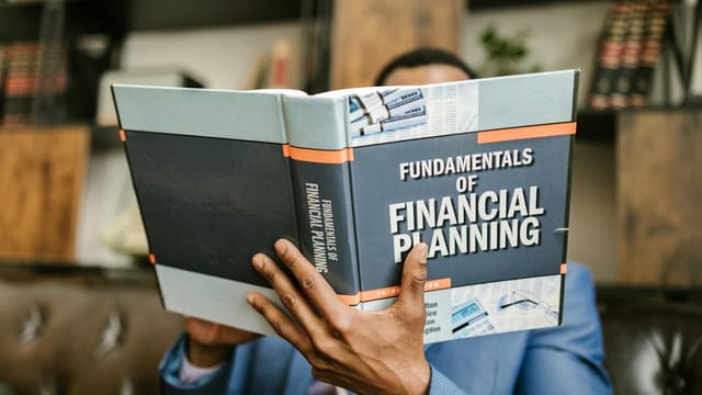 A professional individual in a suit reading 'Fundamentals of Financial Planning' indoors.