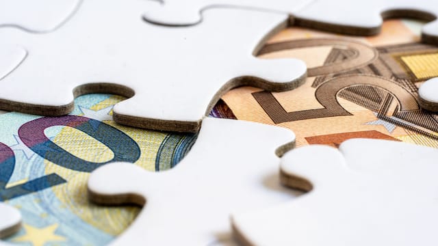 Close-up of euro banknotes revealed under puzzle pieces, symbolizing financial solutions.