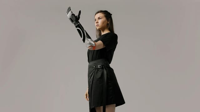 Empowering portrait of a young woman showcasing a futuristic prosthetic arm in a studio setting.
