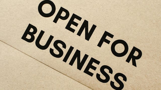 Close-up of an 'Open for Business' sign on a textured brown paper background.