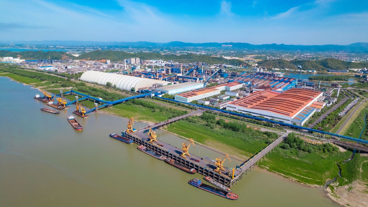 A spacious industrial port with yellow cranes, warehouses, and river access under a clear blue sky.