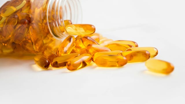 Close-up of fish oil capsules spilling from a bottle on white background.